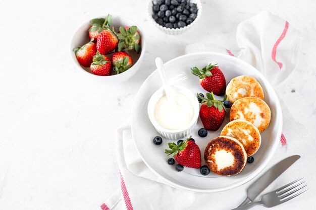 Quark Pfannkuchen Käsekuchen Ricotta Krapfen mit frischen Erdbeeren und Heidelbeeren aus einer weißen Keramikplatte Gesundes und leckeres Frühstück für den Urlaub