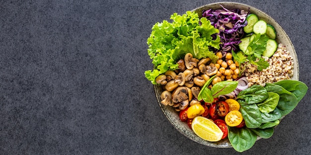 Quinoa, Pilze, Salat, Rotkohl, Spinat, Gurken, Tomaten, eine Schüssel Buddha auf dunkler Draufsicht.