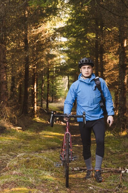 Radfahrer in blauem Mantel und Helm im Park mit hohen Bäumen