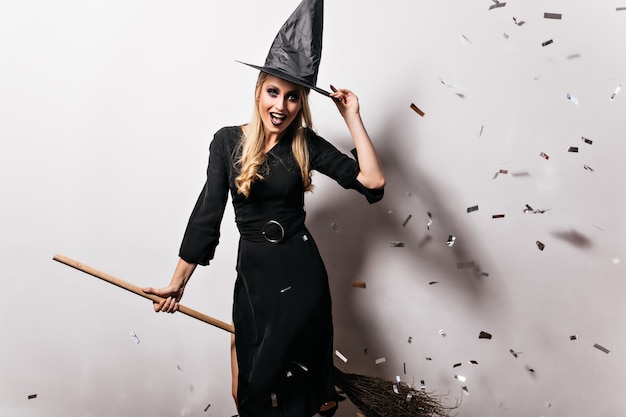 Raffinierte blonde Frau, die im Hexenkostüm posiert. hübsches kaukasisches Mädchen, das Spaß an der Halloween-Party hat.