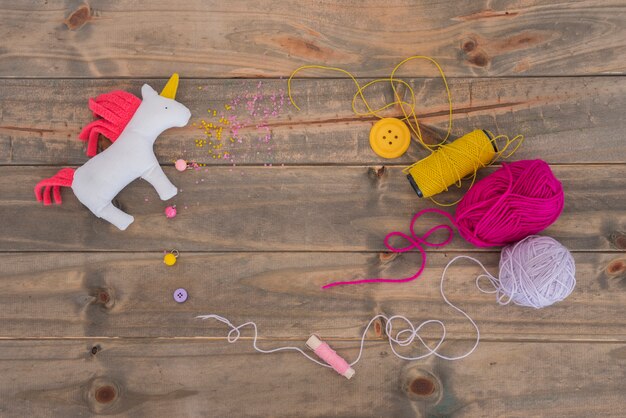 Rag Einhorn Pferd mit Garn; rosa und lila Spule mit Faden und Knopf auf hölzernem Schreibtisch