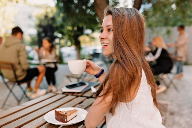 Rahmen von der Rückseite der jungen attraktiven Frau mit dem langen Haar, das Kaffee auf Sommerterrasse in gutem sonnigem Tag trinkt