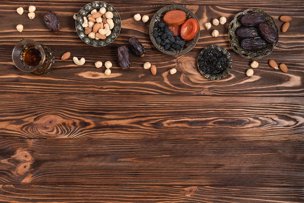 Ramadan frische Datteln; getrocknete Früchte; Nüsse und Kräuterteeglas auf Schreibtisch aus Holz