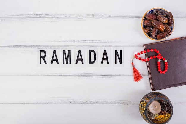 Ramadan-Text mit Schüssel saftiger Datteln; Tagebuch und rote Gebetsperlen auf weißer Tabelle