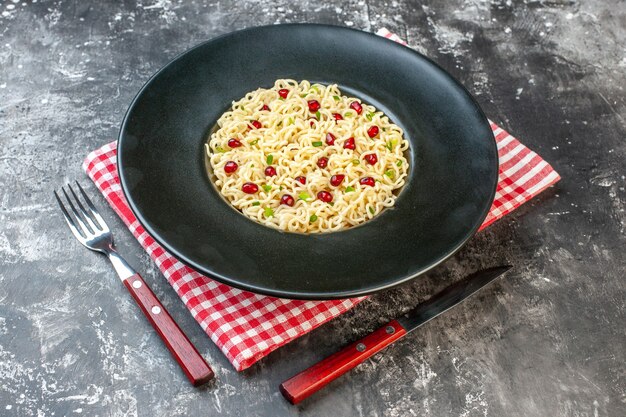 Ramen-Nudeln von unten auf dunkler runder Platte rot-weiß karierte Serviette Gabel und Messer auf dunklem Tisch