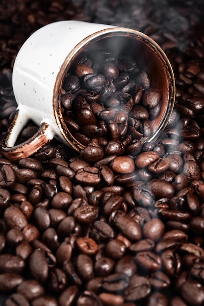 Rauch steigt aus gerösteten Kaffeebohnen Kaffeebecher liegt auf duftendem Kaffee, selektiver Fokus auf Bohnen