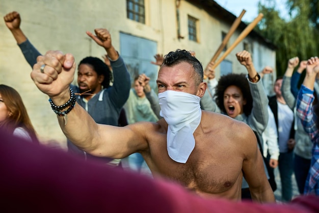 Rebellischer Mann mit Gesichtsmaske protestiert mit Menschenmassen auf den Straßen der Stadt