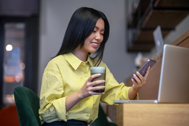 Recht junge asiatische Frau im gelben Hemd, das an einem Laptop arbeitet