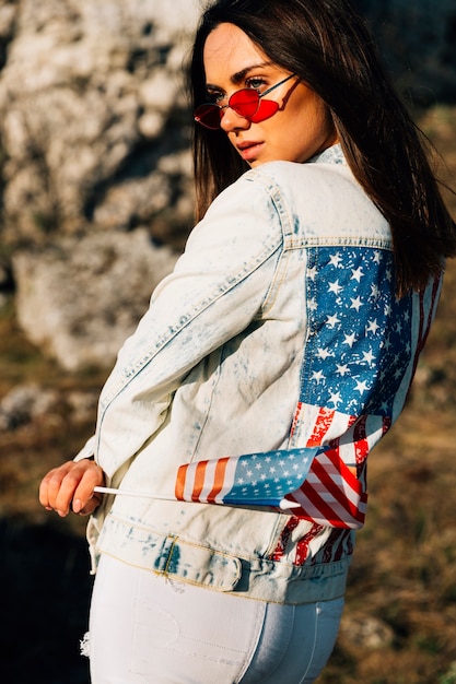 Kostenloses Foto recht junge frau in der denimjacke mit amerikanischer flagge am sonnigen tag