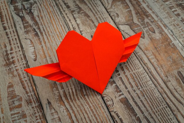 Red Papier Origami-Herz mit Flügeln auf Holz Hintergrund.