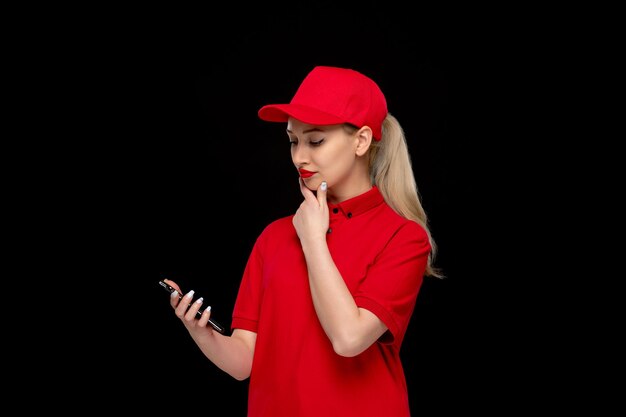 Red Shirt Day süße Frau, die auf den Telefonbildschirm in einer roten Mütze mit Hemd und hellem Lippenstift schaut