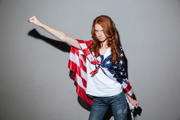 Redhead junge Dame Superheld mit USA Flagge. Kamera schauen.