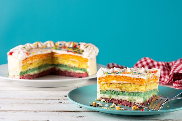 Regenbogen-Schichtkuchen auf weißem Holztisch und blauem Hintergrund