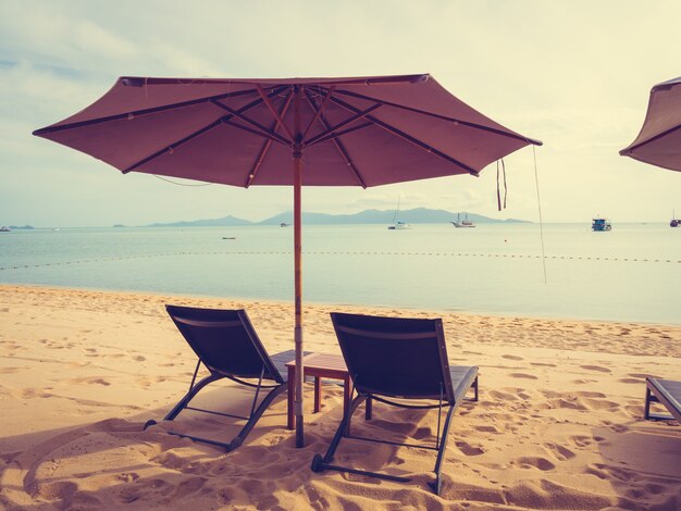 Regenschirm und Stuhl auf dem tropischen Strandmeer und -ozean zur Sonnenaufgangzeit