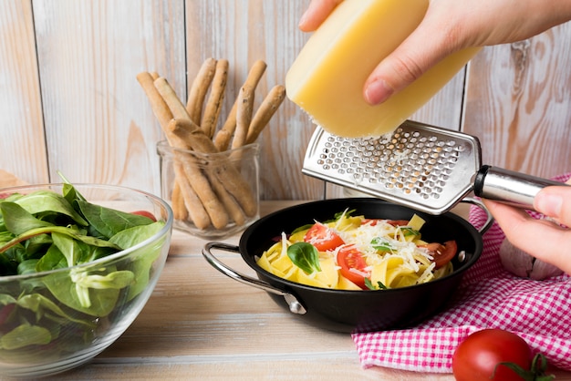 Reibender Käse der Person über frischen gekochten Spaghettis im Behälter mit Gemüse auf worktop