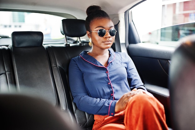 Reiche afrikanische Geschäftsfrau mit Sonnenbrille sitzt im Geländewagen mit schwarzen Ledersitzen
