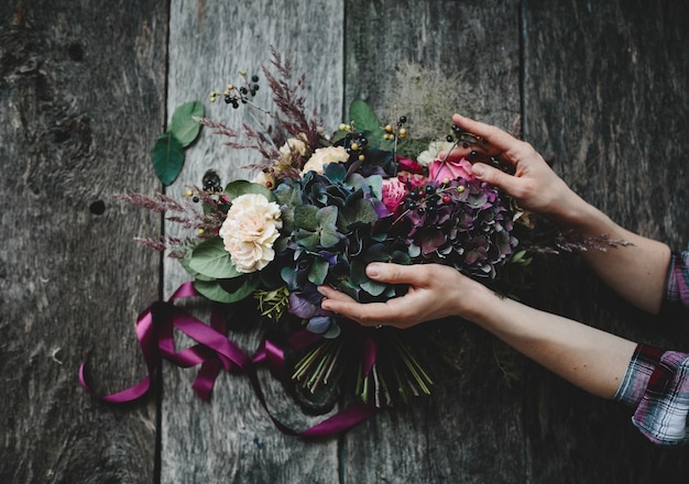 Reicher Blumenstrauß von dunklen Blumen und von weißen Rosen liegt auf Holztisch