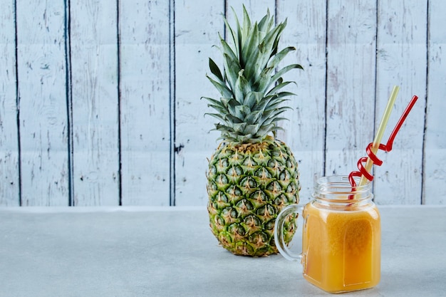 Reife Ananas und ein Glas Saft auf Blau.