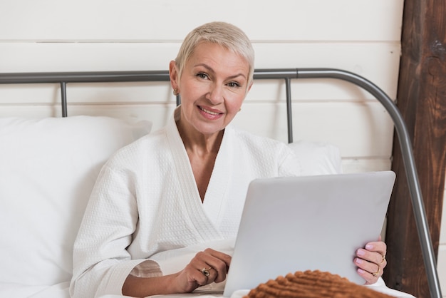 Kostenloses Foto reife frau der vorderansicht, die auf einem laptop im bett schaut