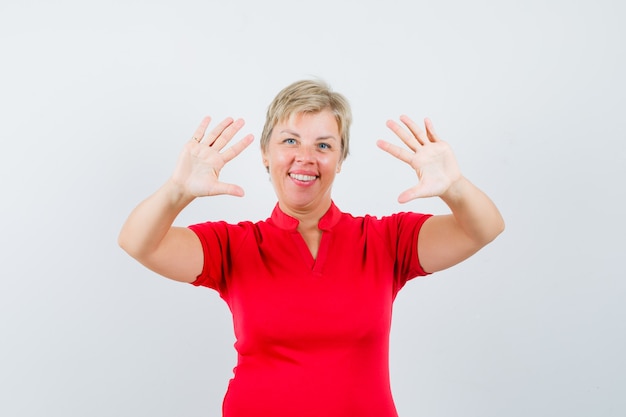 Reife Frau, die Ablehnungsgeste im roten T-Shirt zeigt und fröhlich aussieht.