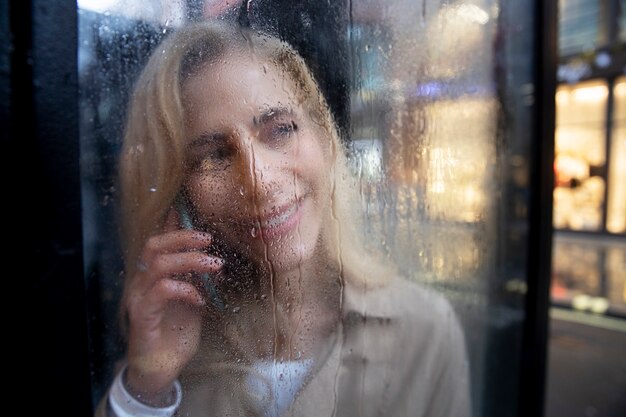 Reife Frau, die am Telefon spricht, während es regnet