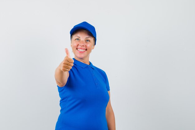 Reife Frau, die Daumen oben im blauen T-Shirt zeigt und fröhlich schaut.