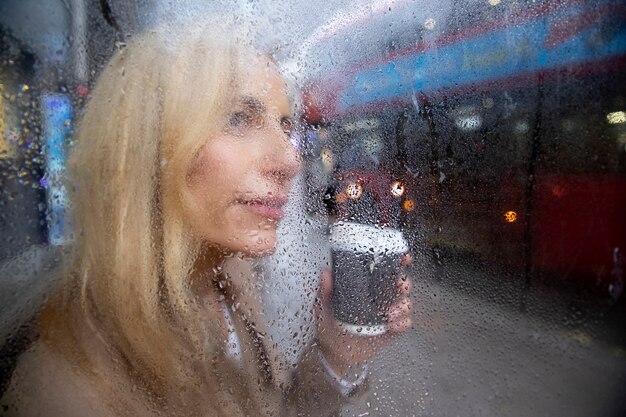 Reife Frau, die draußen einen Kaffee trinkt, während es regnet