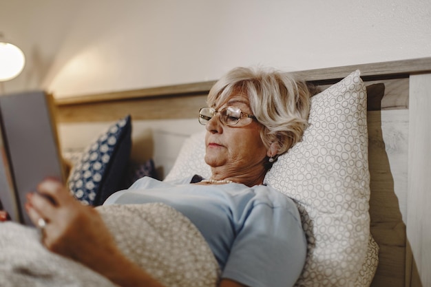 Reife Frau, die ein Buch liest, während sie sich im Bett hinlegt