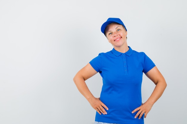 Reife frau, die hände auf taille im blauen t-shirt hält und zuversichtlich schaut