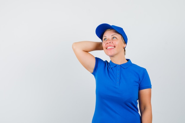 Reife Frau, die Hand am Hals im blauen T-Shirt hält und verträumt aussieht.