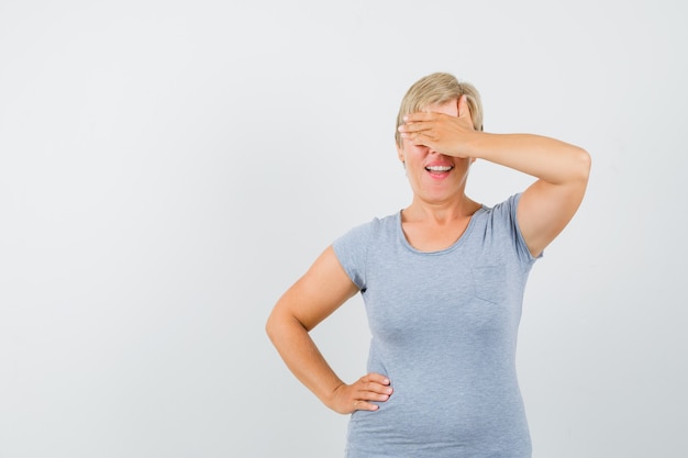 Reife Frau, die Hand auf Augen im grauen T-Shirt hält und neugierig schaut