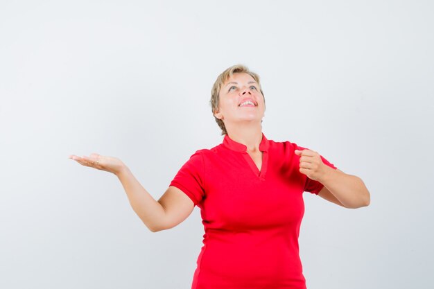 Reife Frau, die Handfläche beiseite spreizt und vorgibt, etwas im roten T-Shirt zu halten