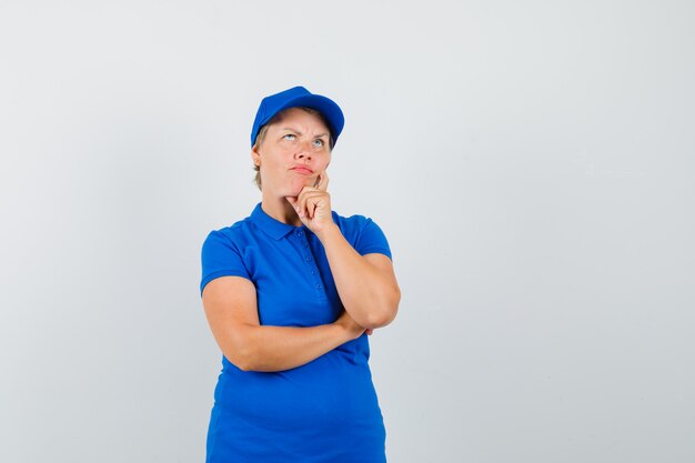 Reife Frau, die Kinn auf Hand im blauen T-Shirt stützt und zögernd schaut