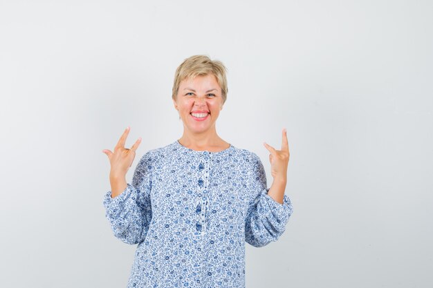 Reife Frau, die Rock'n'Roll-Geste im Hemd zeigt und glücklich schaut