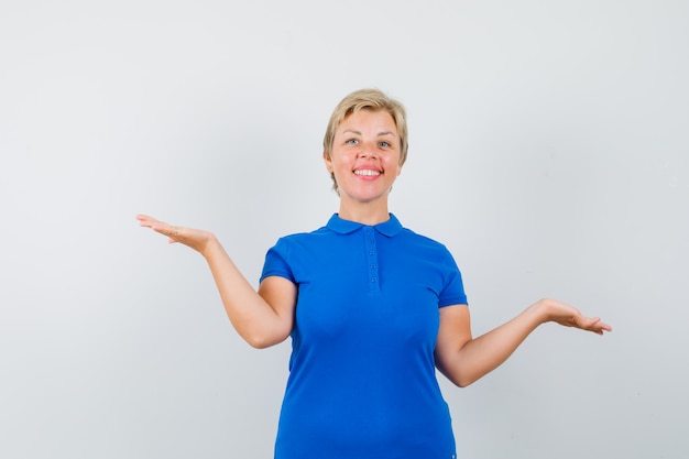 Reife Frau, die Schuppengeste im blauen T-Shirt macht und froh aussieht.