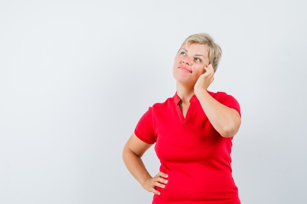 Reife Frau, die vorgibt, auf Handy in rotem T-Shirt zu sprechen und nachdenklich aussieht