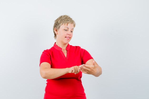 Reife Frau, die vorgibt, Handy im roten T-Shirt zu benutzen und beschäftigt schaut