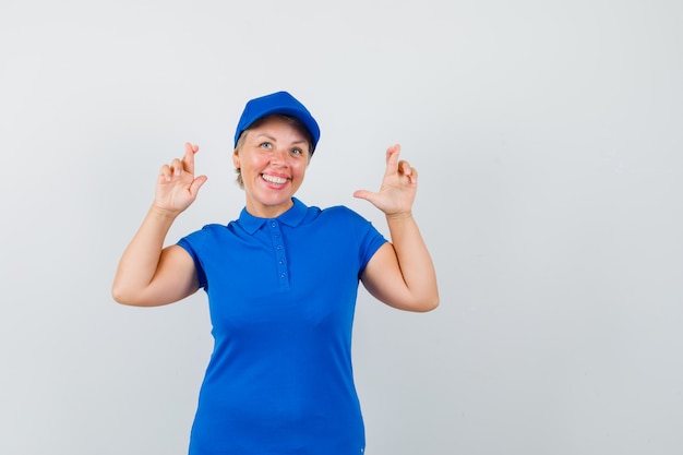 Reife Frau drückt die Daumen im blauen T-Shirt und sieht gemütlich aus