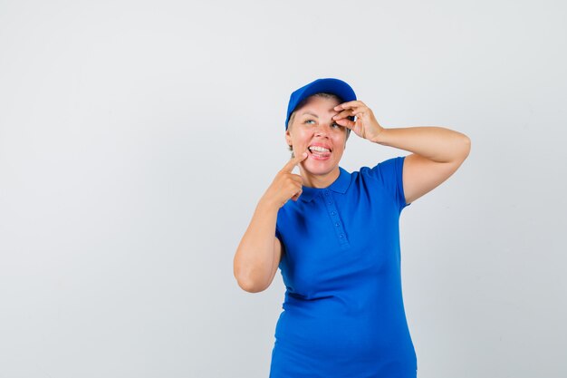 Reife Frau im blauen T-Shirt, das ok Zeichen zeigt, Zunge herausstreckt und fröhlich aussieht