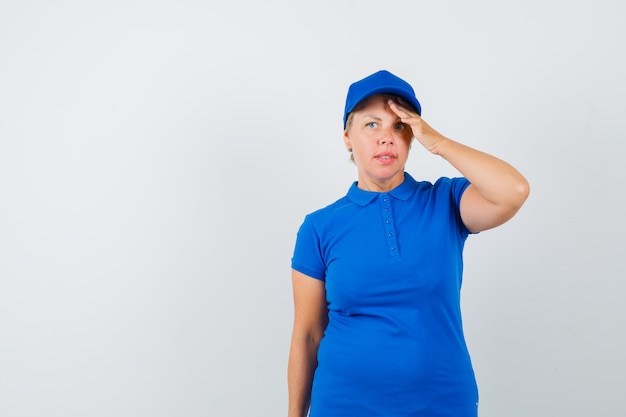 Reife Frau im blauen T-Shirt, die Hand über Stirn hält und nachdenklich schaut.