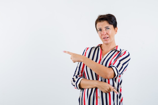 Reife Frau in gestreifter Bluse zeigt mit Zeigefinger nach links und rechts und sieht ernst aus, Vorderansicht.