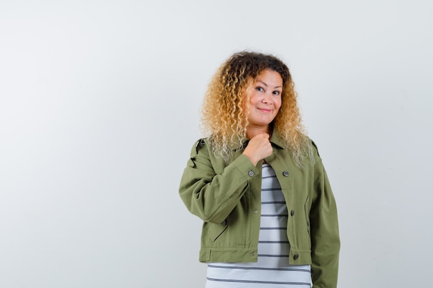 Reife frau in grüner jacke, t-shirt, das hand auf brust hält und fröhlich schaut, vorderansicht.