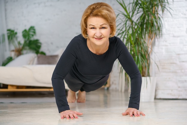 Reife Frau in schwarzer Sportbekleidung, die zu Hause Liegestütze macht. Gesundes Lebensstilkonzept