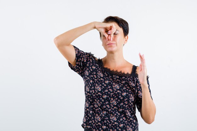 Reife Frau kneift die Nase wegen schlechten Geruchs in Blumenbluse, schwarzem Rock und sieht gereizt aus. Vorderansicht.