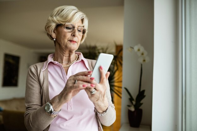 Reife Frau mit Handy und Textnachricht zu Hause lesen