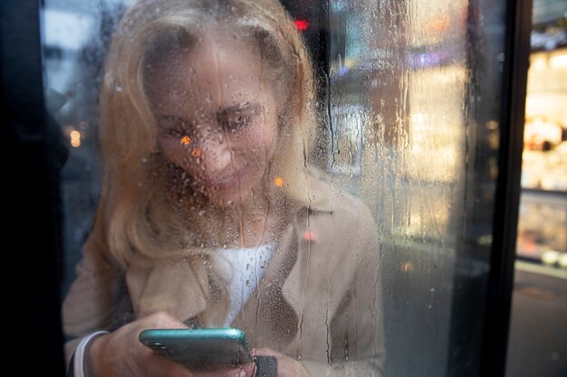 Reife Frau SMS am Telefon, während es regnet