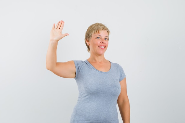 Reife Frau winkt Hand, um sich im grauen T-Shirt zu verabschieden und froh auszusehen