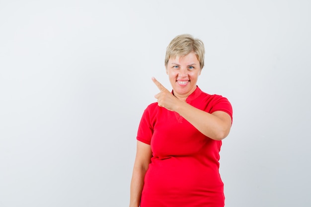 Reife Frau zeigt auf die obere linke Ecke im roten T-Shirt und sieht froh aus.