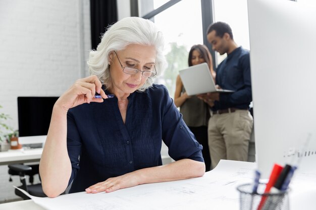 Reife Geschäftsfrau, die mit Dokumenten arbeitet, während sie an ihrem Arbeitsplatz sitzt