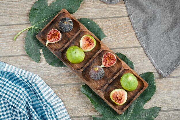 Reife grüne und schwarze Feigen auf Holzplatte mit Blatt und Tischdecken.